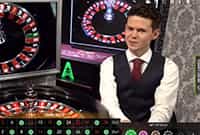 Un crupier de un casino online en vivo junto a una mesa de ruleta.
