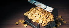 Un cofre con la tapa abierta a rebosar de monedas de oro muy brillantes. 