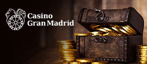 Un cofre lleno de monedas de oro con el logo de Casino Gran Madrid a la izquierda.
