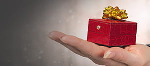 Una persona sosteniendo sobre la palma de la mano una pequeña caja con un lazo de regalo.