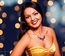 Primer plano de una crupier morena con un vestido dorado y los labios pintados de color oscuro sonriendo a cámara.