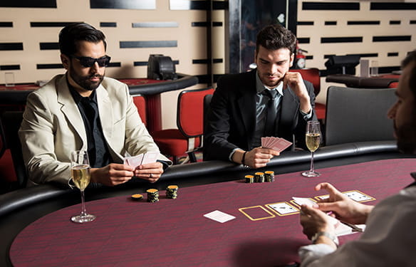Dos hombres vistiendo chaqueta y corbata jugando al póker y tomando champagne.