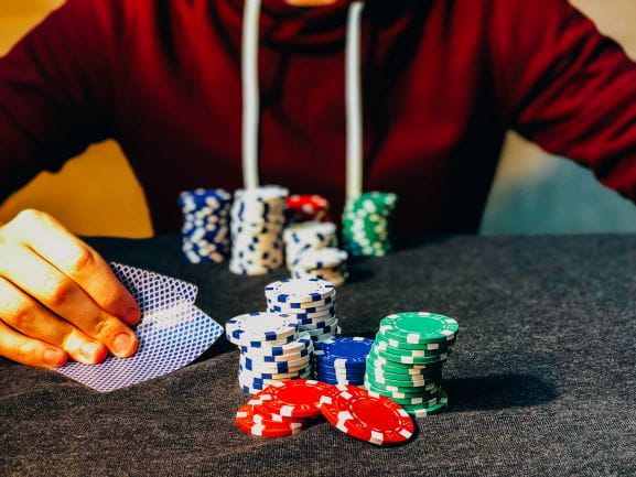 Una mano sostiene dos cartas de póker con fichas sobre una mesa.