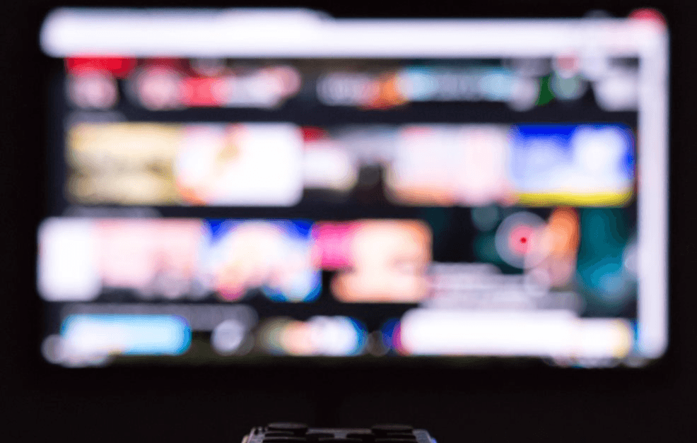 Un mando de televisión apuntando hacia una pantalla difuminada.