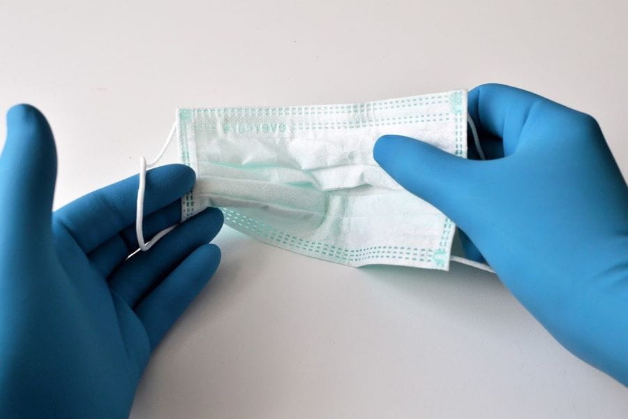 Dos manos con sendos guantes azules sostienen una máscara de protección sanitaria.