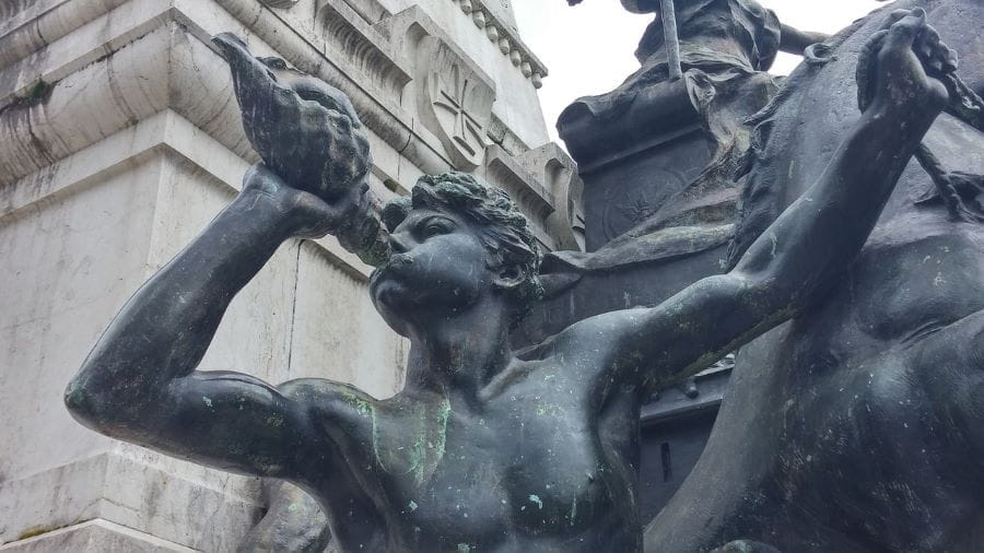 Fragmento de una estatua pública con una figura soplando una concha.