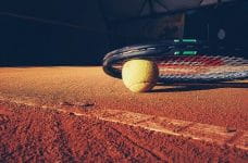 Raqueta y pelota de tenis en una pista de tierra batida.