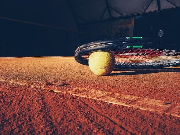 Raqueta y pelota de tenis en una pista de tierra batida.