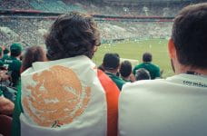 Aficionado al fútbol envuelto en una bandera mexicana.