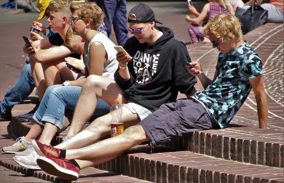 Un grupo de adolescentes, sentados en unos escalones de una plaza, usan su teléfono móvil sin mirarse entre ellos.