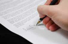 Persona firmando con pluma un documento legal.