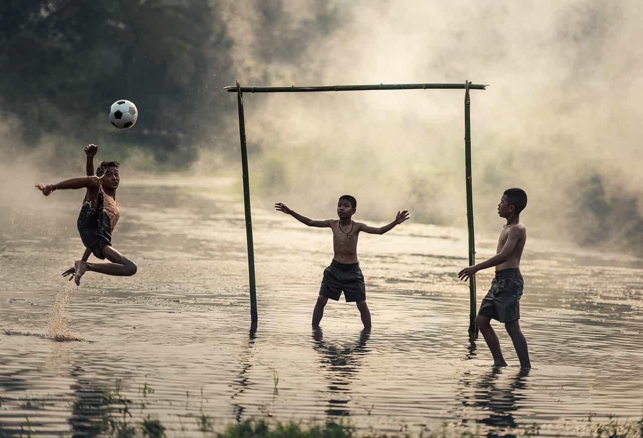 Tres niños jugando al fútbol en un precario gramado.