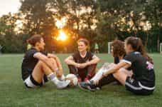 Cuatro jugadoras de fútbol sentadas en el cesped del campo.