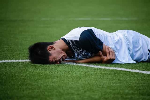 Futbolista tumbado en el campo con gesto de dolor.