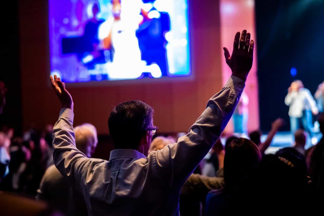 Persona entre el público de una sala con los brazos levantados en gesto de alegría.