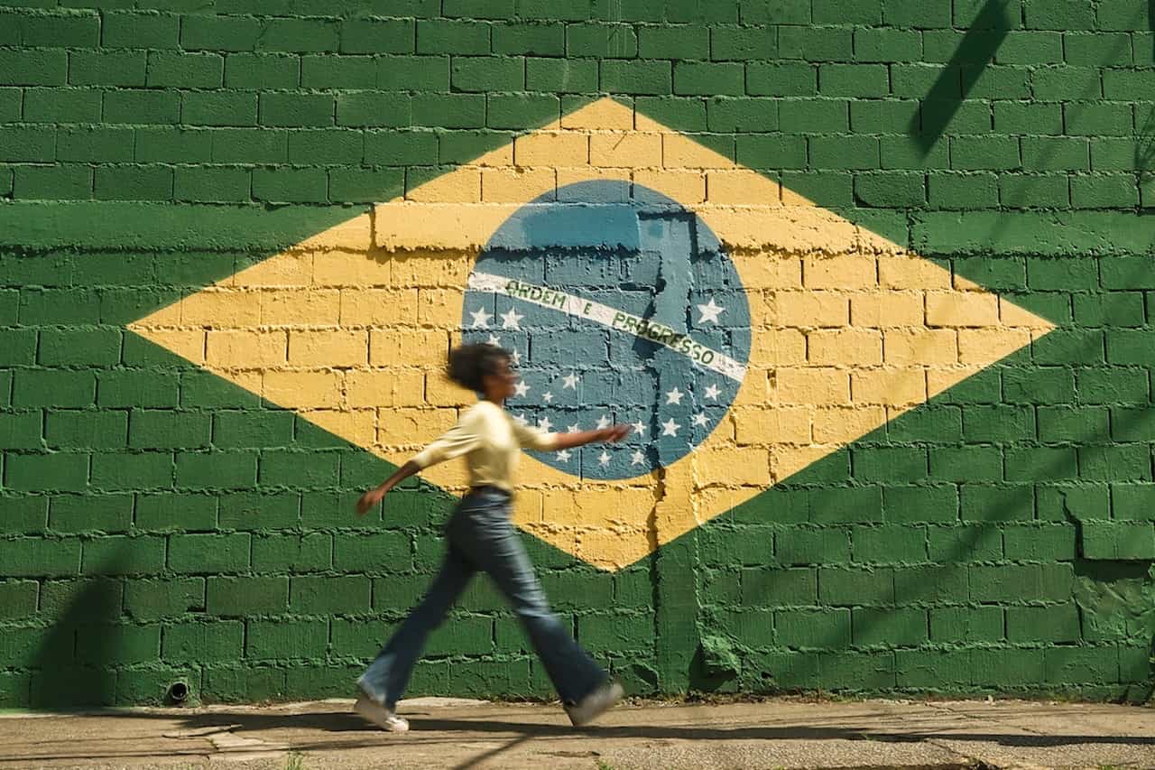 Chica brasileña pasando por delante de una pared pintada como la bandera de Brasil.