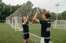 Dos jugadoras de fútbol en el campo con gesto de chocar las manos.