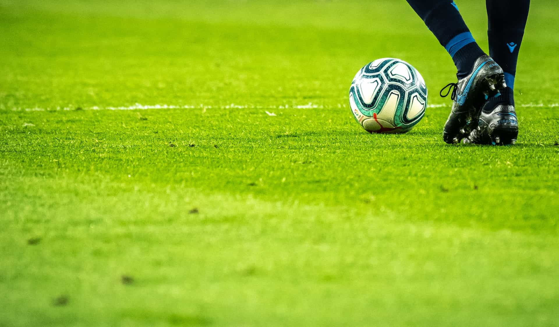 Pies de un futbolista junto a un balón en un campo de fútbol.