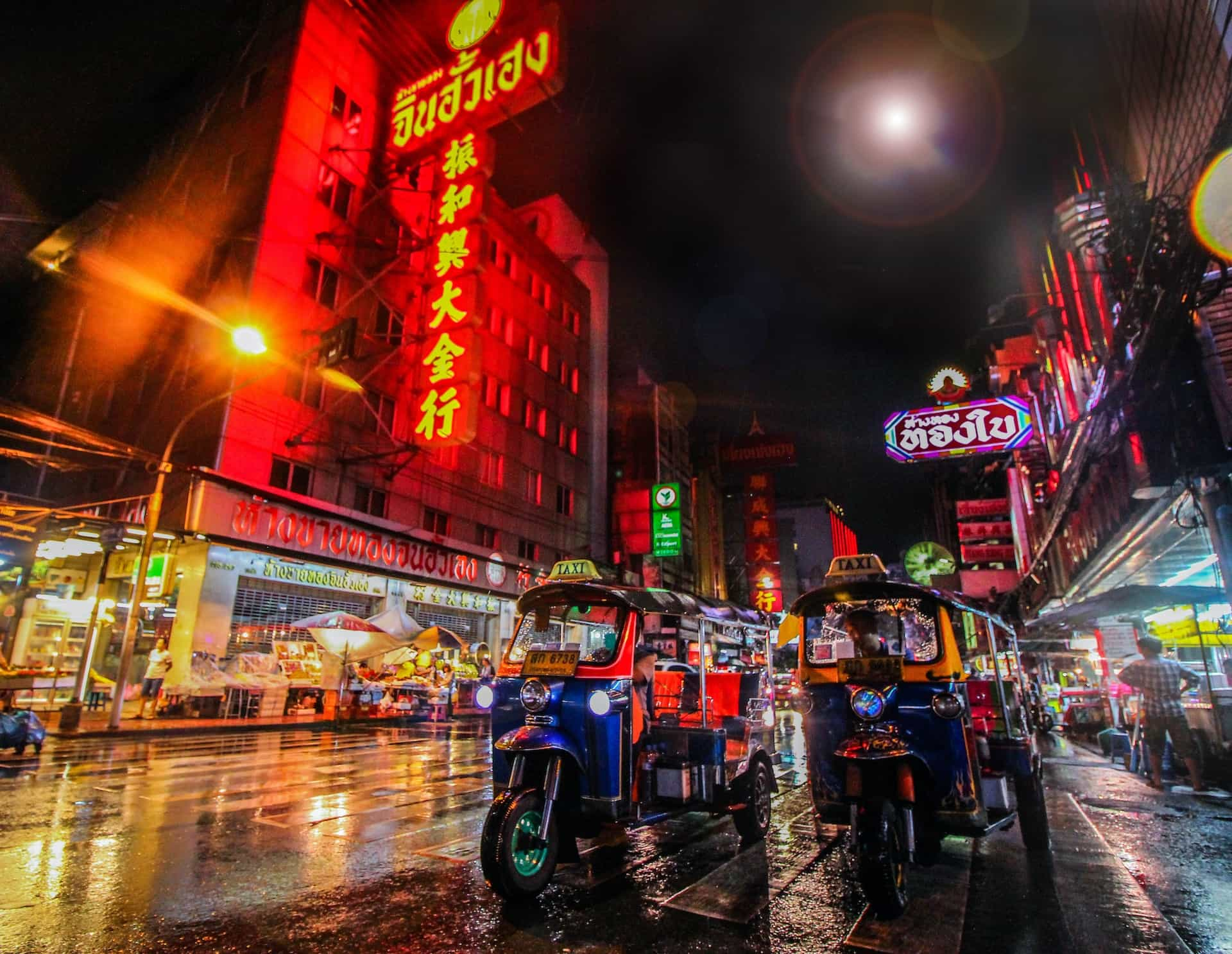 Edificios luminosos y dos tuk-tuk en una calle de la ciudad de Bangkok (Tailandia).