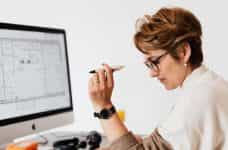 Mujer con un bolígrafo en la mano mirando informes frente a un ordenador.