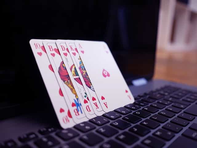 Cuatro naipes apoyados en la pantalla de un ordenador portátil.