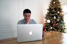 Chico sentado frente a su ordenador portátil junto a un árbol de Navidad.