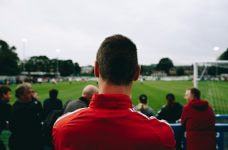 Hombre de espaldas mirando un partido de fútbol desde la grada.