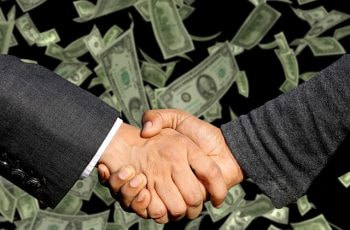 Apretón de manos entre dos empresarios sobre una lluvia de billetes.