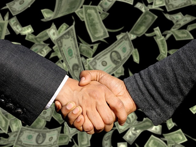 Apretón de manos entre dos empresarios sobre una lluvia de billetes.