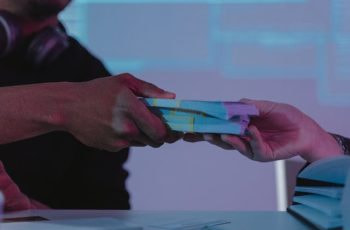 Dos personas pasándose varios fajos de billetes.