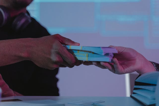 Dos personas pasándose varios fajos de billetes.