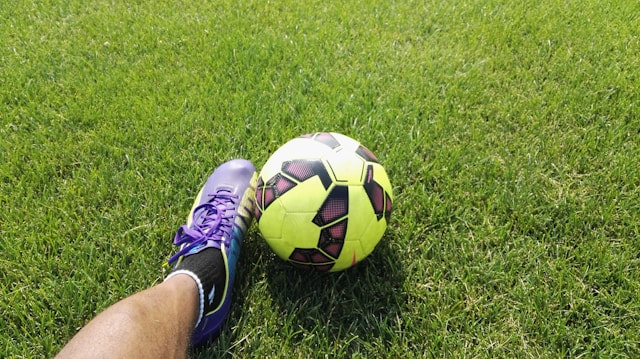 Balón de fútbol junto al pie de un futbolista en el campo de juego.