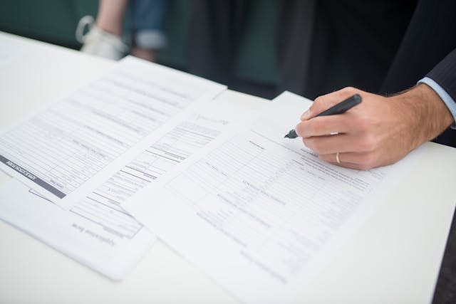 Mano de un hombre firmando varios documentos.