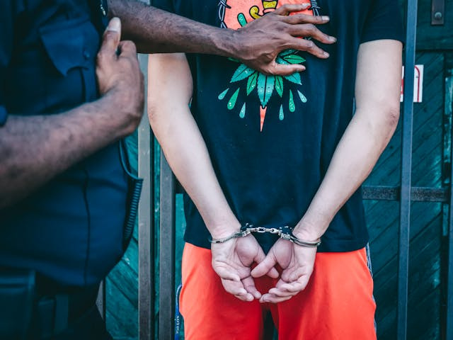 Hombre de espaldas esposado junto a un policía.
