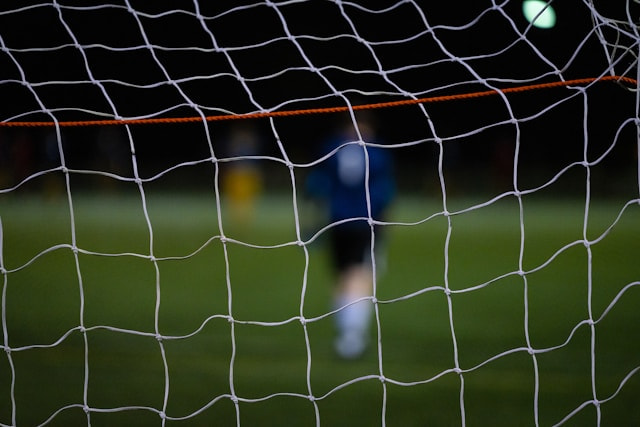 Red de una portería de fútbol con el portero difuminado al fondo.