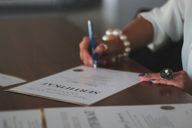 Mujer firmando un diploma sobre una mesa.