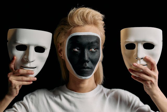 Mujer con la cara pintada de negro sosteniendo dos máscaras.