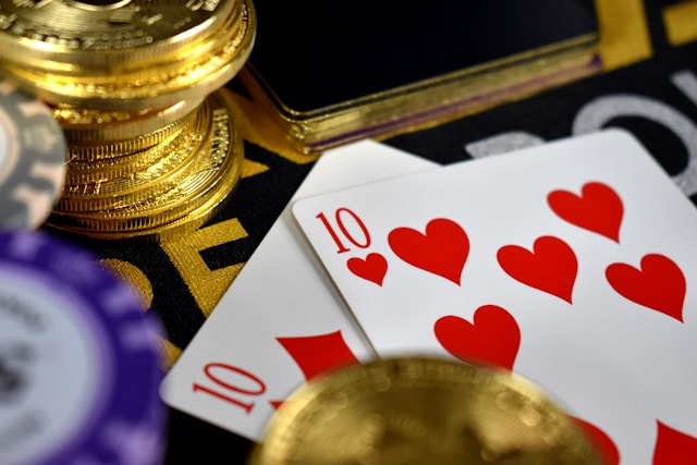 Cartas de póker junto a unas monedas doradas sobre un tapete.