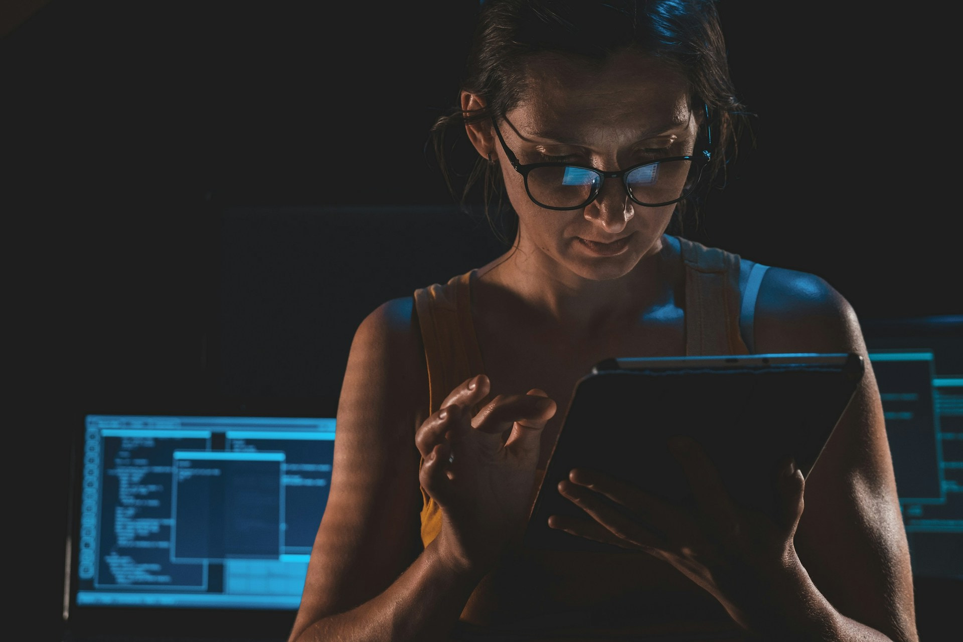 Mujer con gafas usando una Tablet en una sala con ordenadores.