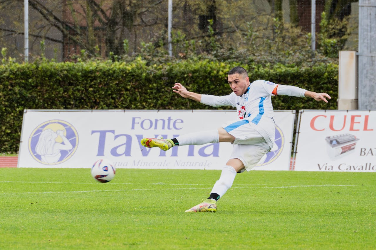 Jugador de fútbol pateando un balón en el campo durante un partido.