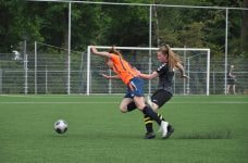 Dos jugadoras de fútbol tropezándose entre sí mientras corren por el campo detrás del balón.
