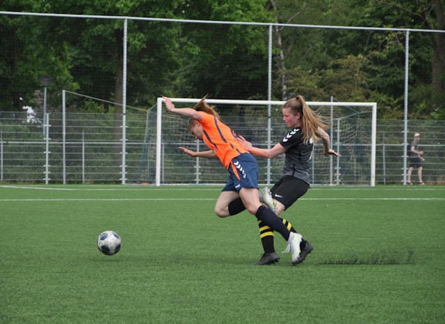 Dos jugadoras de fútbol tropezándose entre sí mientras corren por el campo detrás del balón.