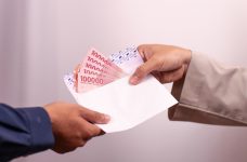 Dos manos sujetando un sobre abierto con billetes en su interior.