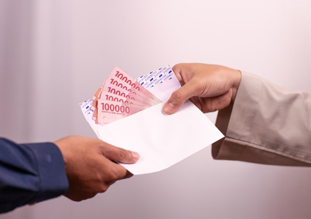 Dos manos sujetando un sobre abierto con billetes en su interior.