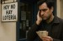 Hombre preocupado con boletos de lotería frente a cartel que dice “Hoy no hay lotería”.