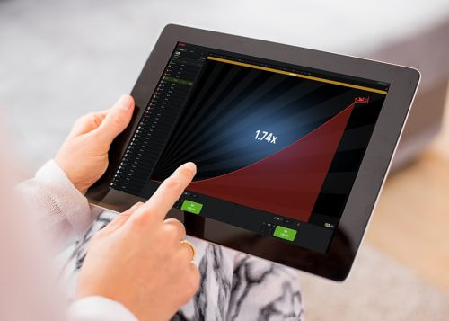 Mano sosteniendo una tablet con el juego Aviator en pantalla mostrando el multiplicador de apuesta.