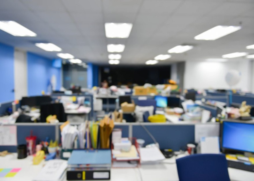 Oficina con escritorios desenfocada bajo iluminación fluorescente.