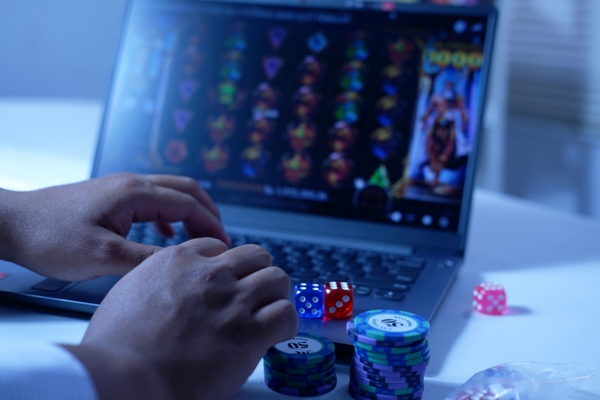 Manos frente a portátil con tragaperras y fichas y dados sobre la mesa.