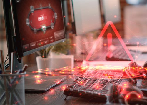 Teclado y ordenador con icono de alerta roja y pantalla de póker.