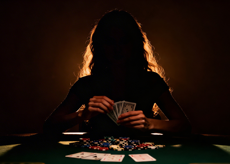Mujer jugando póker con cartas en la mano y fichas sobre la mesa.